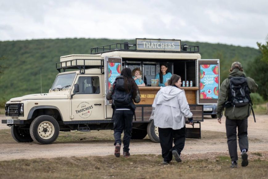 a truck saying thatchers on the side of a path, people walking up to it